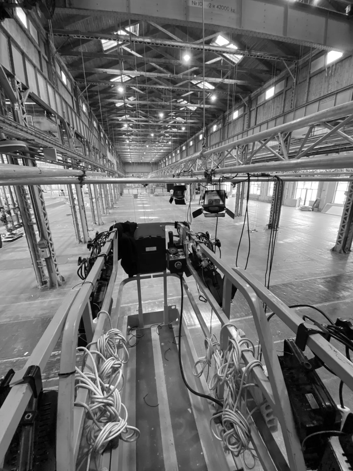 View from a lift platform with lights rigged along a truss inside a large industrial hall